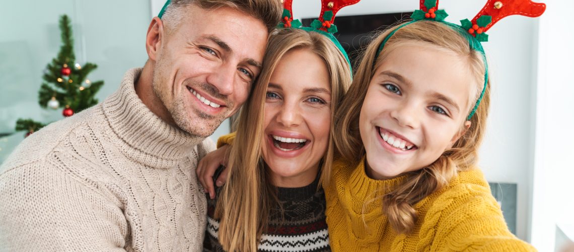 Image of caucasian happy family in Christmas reindeer antlers celebrating holiday at home with New Year tree
